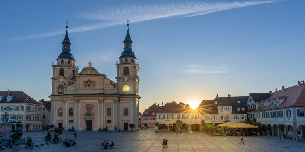Blick auf den Marktplatz im Vordergrund Menschen, im Hintergrund die evangelische Stadtkirche und die letzten Sonnenstrahlen am Abend